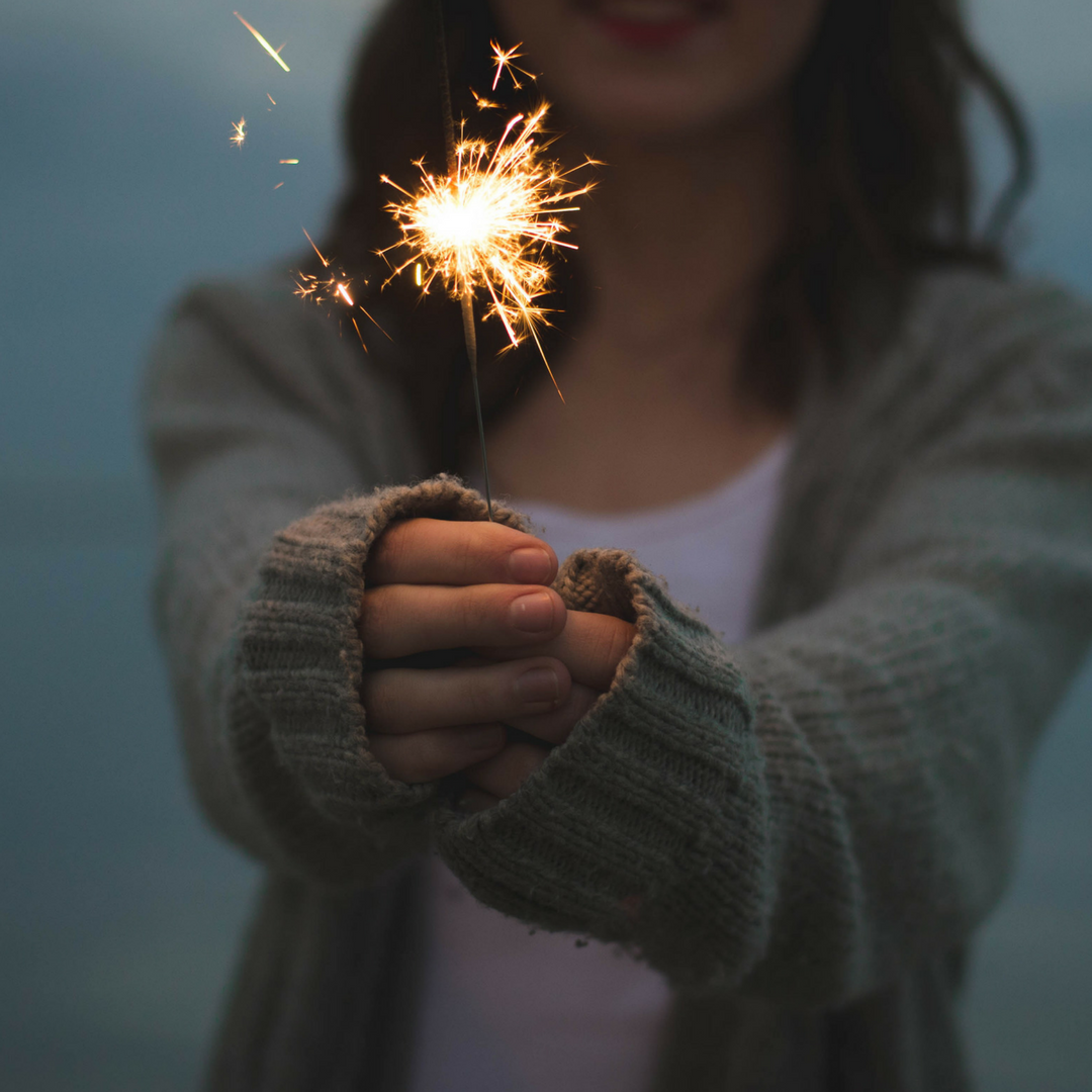 a woman in a sweater holding a lit sparkler